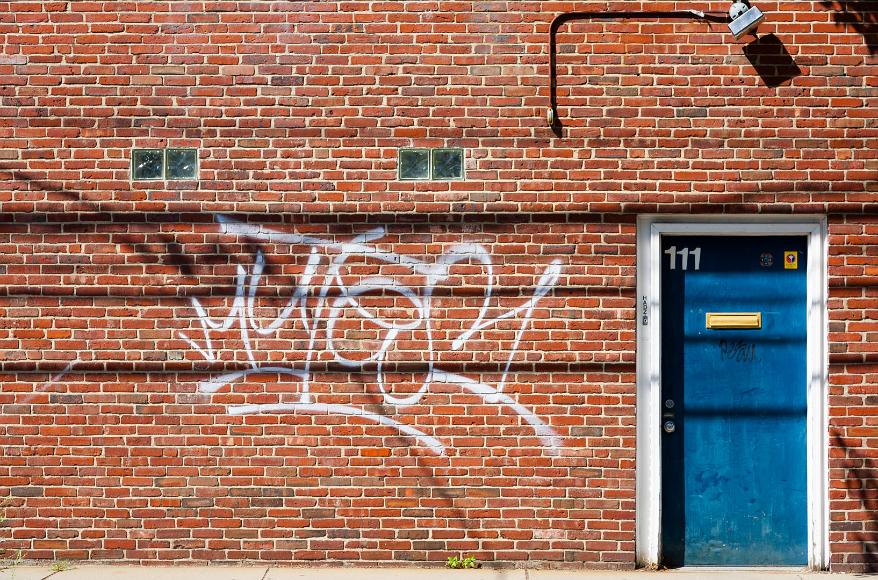 Graffiti wallscape Cambridge Massachusetts Painted graffiti on a red brick wall with a blue door with the number 111, a mail slot, and also has graffiti on it, all brightly sunlit, East Cambridge, MA...
