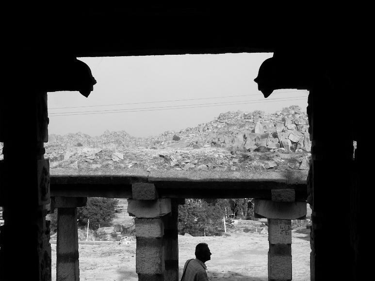 Man framed by old temple in Hampi Man framed by the silhouette of ruined temples composed on massive old carved stone from the ruins of Vijayanagara in Hampi, Karnataka, India
