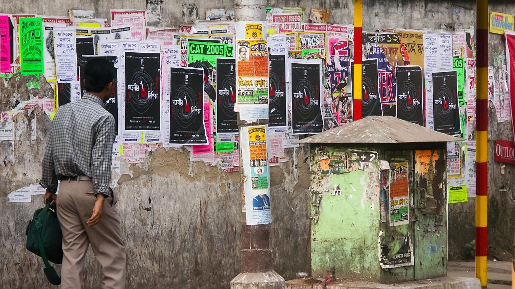 Man walking in front of posters in Kolkata a man with a green business satchel walks along a sidewalk in front of a wall with various posters pasted to it in Calcutta India