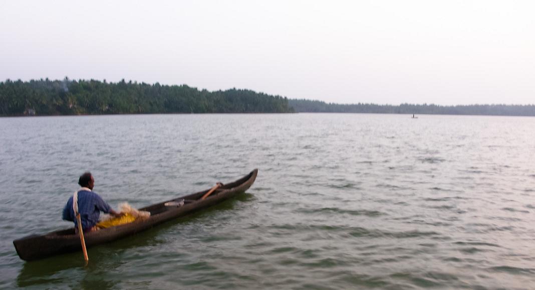 Paddling a canoe out into the backwaters of Kerala A man steadies his load with one hand while paddling his canoe with the other along the backwaters of Kerala, India