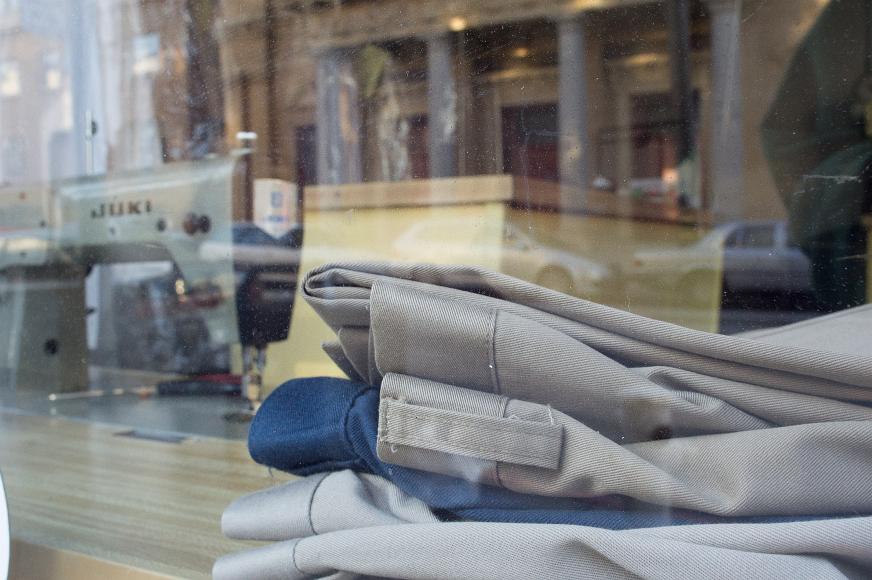 Pants window Three pairs of pants and a sewing machine are visible through a shop window that is also reflecting the street scene outside.