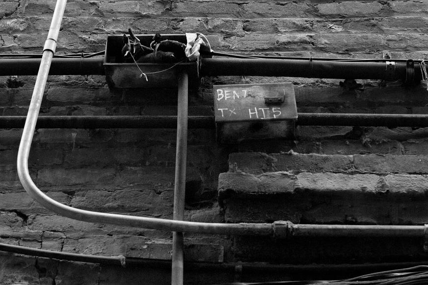 Chinatown wall detail #3 Black and white image of pipes wires and conduits snaking across an older brick wall