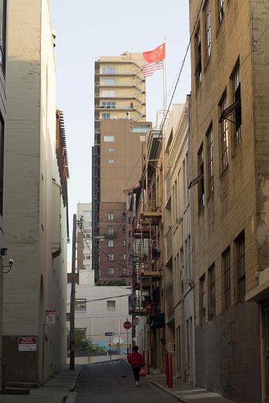 Woman walks down a Chinatown street Woman walking down a narrow side street underneath large brick buildings one of which is sporting Chinese and Smerican flags with the Chinese flag on top