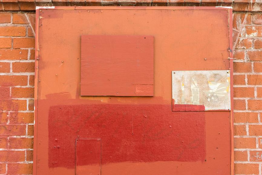 Chinatown wall detail #2 Red painted wooden board with still slightly visible graffiti painted over in various shades on red on top of a red brick wall