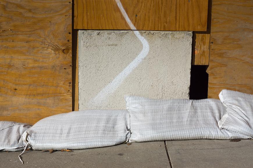 Four Sandbags sandbags on a sidewalk in front of stucco and plywood sheeting