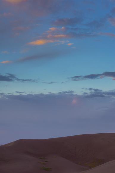 Sunrise at the Great Sand Dunes Beige sand dunes with yellow and green small plants underneath a sunrise sky near Alamosa Colorado