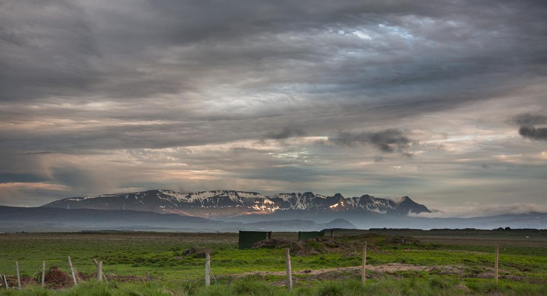 Mountain peaks in Iceland Snow and rock covered mountain lay behind green fields and fences under a cloudy sky