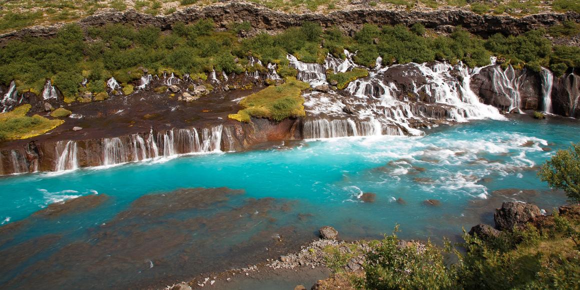 Hraunfossar waterfall in Iceland Turquoise blue waters tumble from the middle of a porous volcanic flow seemingly coming from the middle of a cliff