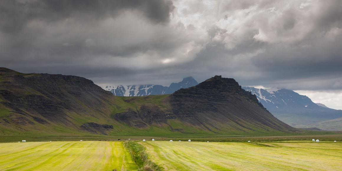 Hayed fields and mountains in Iceland Bright green recently cut fields with haybales wrapped in white plastic visible behind with black volcanic hills and mountains behind