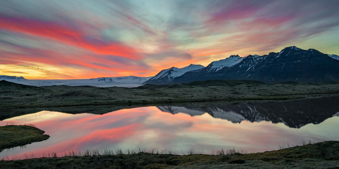 Sunset reflections Pink and Orange clouds after sunset glow in the sky and reflected upon a still pool in the foreground, with snow covered mountains and a glacial toungue down...
