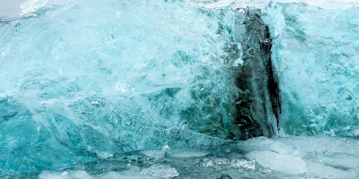 Blue ice, old carbon deep blue ice from a glacier swims in Jokulsarlon pond with a slash of dark lava dust carved from its course to the sea