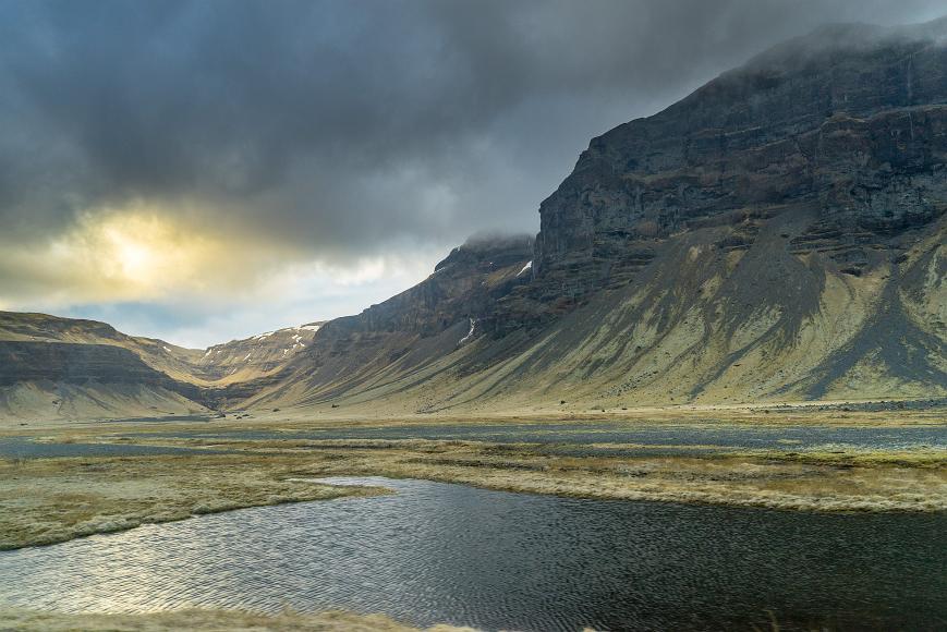 Lake and light High volcanic cliffs with a bit of snow and dramatic clouds and light shining down and reflecting off the water