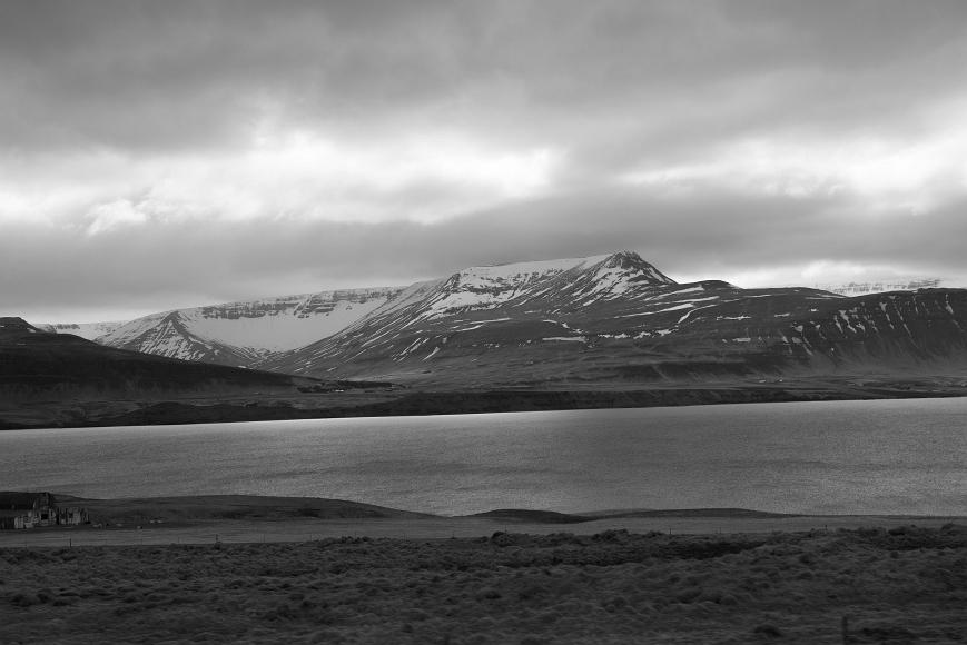 Mountains, fjords, sheeps Old buildings, sheep, fjord, mountains topped with snow, tips in clouds, streams of light onto the water and sky