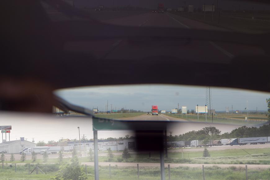 Across flat America - big red truck gonna come for you Flying J truck stop with lots of trucks seen through the windshield of a car driving along the highway with the reflection of a big red truck and other cars and...