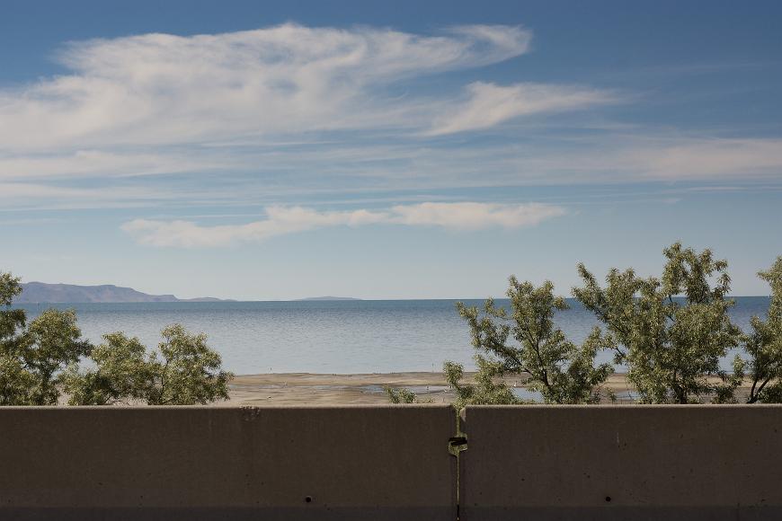 The Great Salt Lake off of I-80 in Utah cocrete dividers in front of small scraggly bushes in front of a lake in front of desert mountains