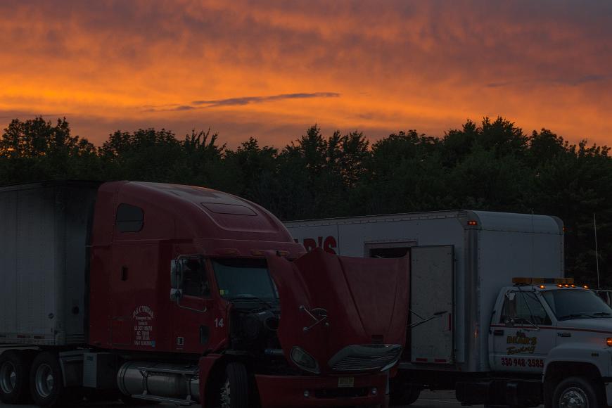Sunset over a truck stop Red truck with its hood up and a tow truck in front of orange clouds at sunset somewhere in middle America