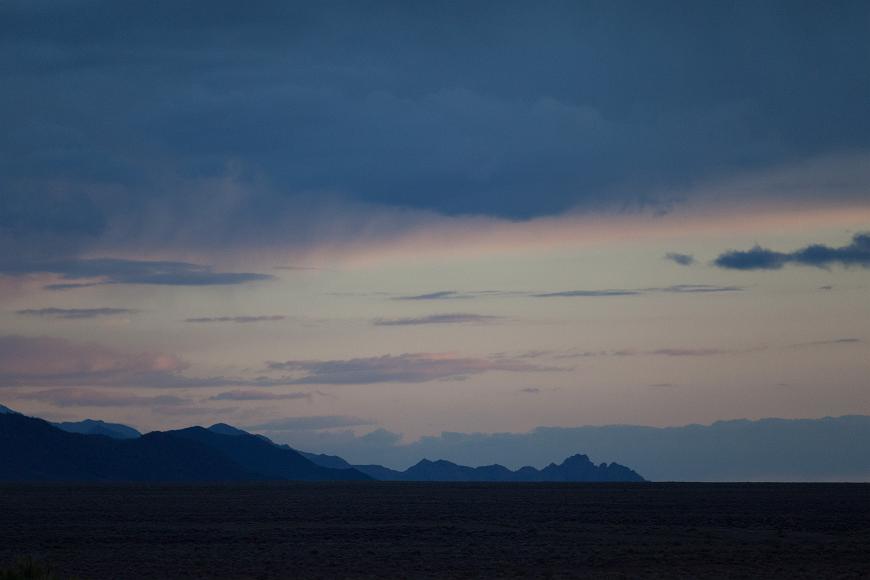 Dusk and a stray storm over jagged mountains in Nevada A storm passes over jagged mountains in the distance above a brown and featureless plain