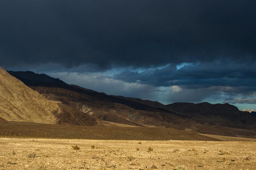 Heavy black clouds over sunlit hills Dark Gray clouds above a stark sunlit desert valley