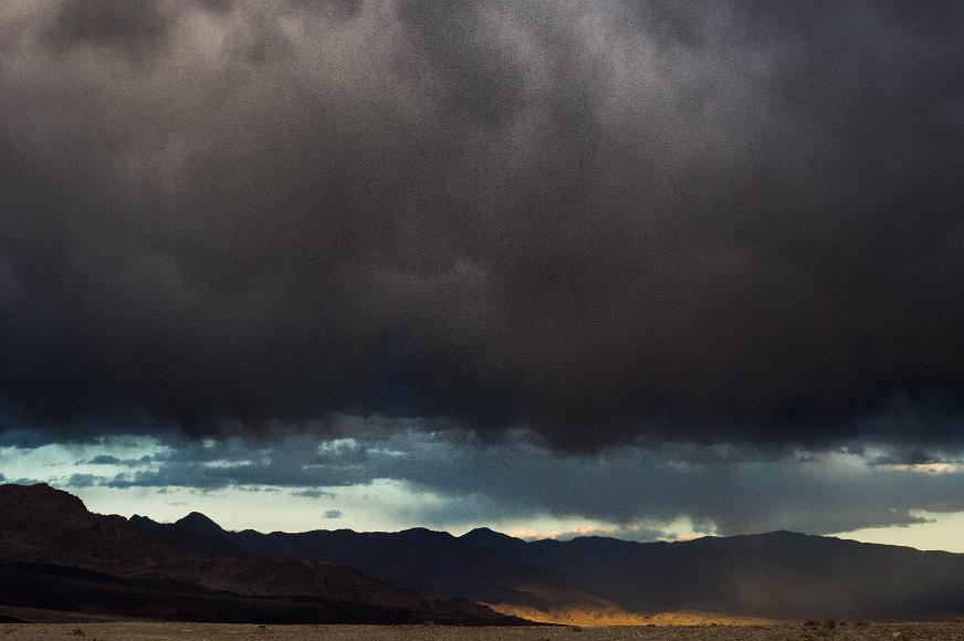 Heavy black clouds over sun dappled desert mountains Dark gray clouds above a sun dappled harsh desert valley