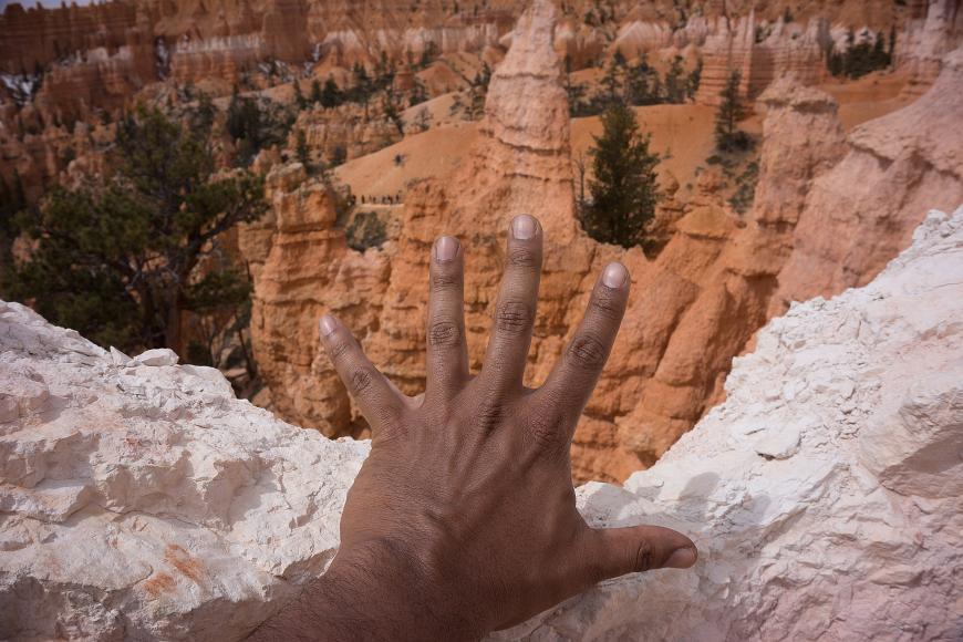 Bryce Canyon and my left hand brown hand in front of pink and orange sandstone hoodoos