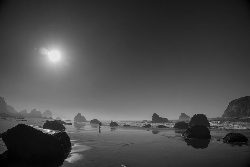 Kat and the Sea Stacks Tiny figure silhouetted against a wet shiny beach and many rocks in black and white