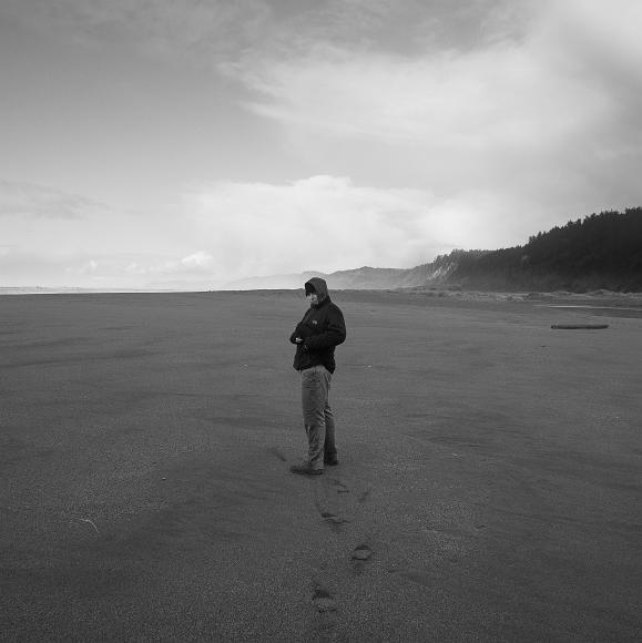 Well insulated sherene looks back on gold bluffs beach A woman in a hoodie and fleece looks back at the camera, her tracks on the beach visible below crasing waves and a stormy sky