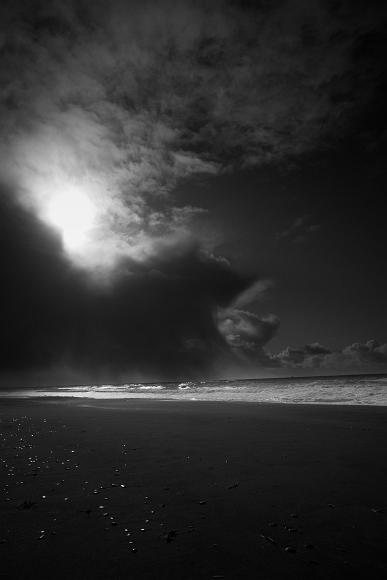 Storm and sun on gold bluffs beach Clouds rain and fog over crashing waves in both sun and shadow and a dark sandy beach strewn with brightly shining pebbles in Jebediah Smith State Redwood Park...