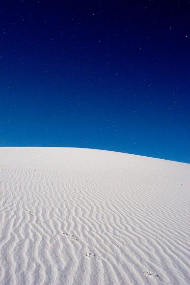 This is a strange and wonderful world we live in. Stars in the deep blue and purple sky above a rippled footstep laden white gypsum sand dunes in White Sands National Monument in New Mexico