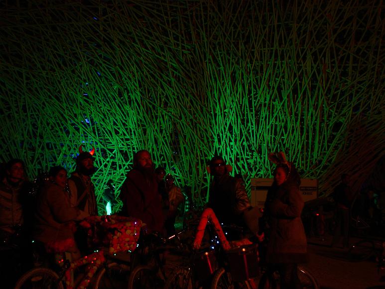 Burning Man 2006 red lit people in costume People in front of a green lit haphazard wooden structure look beyond and behind the viewer
