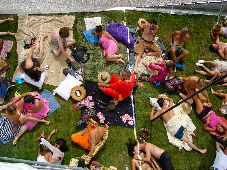 The view from the platform atop Shady Asylum at Burning Man 2006 Many people in colorful outfits stretched out on an enclosed lawn with blankets, many hugging or napping together as viewed from above