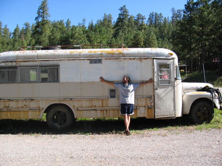 Chris can fly A man stands with arms outstretched in front of an rusty decrepit bus