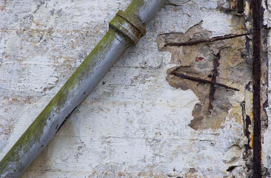 Pipe and metal support Gray pipe with green moss growing on it at a diagonal to a wal with peeling paint and exposed and rusting steel metal rebar at Alcatraz Island Prison National...