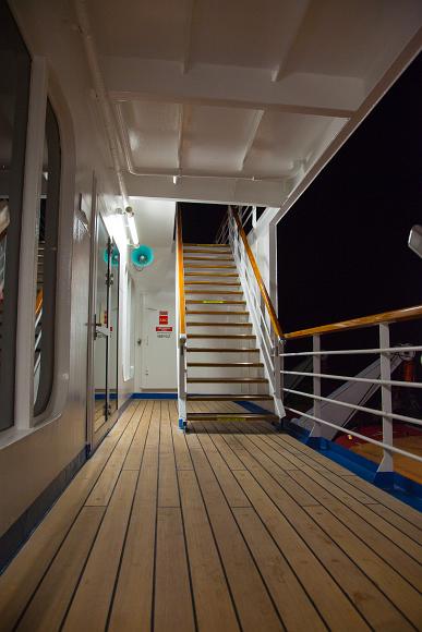 Deck and stairs on a Carnival cruise ship at night Wooden deck with wooden stairs and white metal walls on the outside deck of a cruise ship with darkness all around
