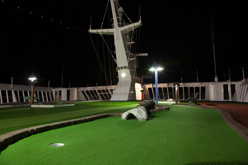 Minigolf course and Communications tower at night on a Carnival Cruise ship the green of artificial turf comprising an empty 9 hole minigolf course with a communications tower in background and a wall around the top deck behind that at...