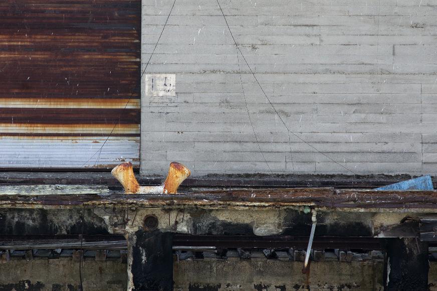 San Francisco Pier Detail #3 pier with concrete wall and rusted bird crap marked metal door with crumbling dock below and wires stretching diagonally towards the dock