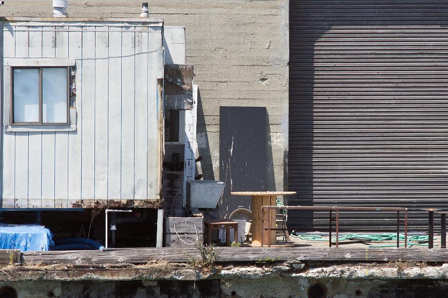 San Francisco Pier Detail #10 trailer boxes random knick knacks with hose and courrgated metal door above a crumbling dock with plants growing out of it